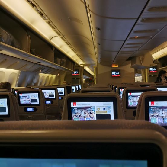 Das Innere eines Flugzeugs zeigt Reihen von Sitzen mit persönlichen Bildschirmen. An der Rückseite jedes Sitzes sind Monitore befestigt. Die Kabine ist gut beleuchtet.