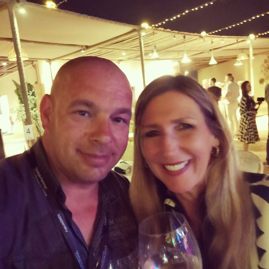 Ein Mann und eine Frau lächeln für ein Selfie bei einer Outdoor-Veranstaltung mit Zelt und Lichterketten.