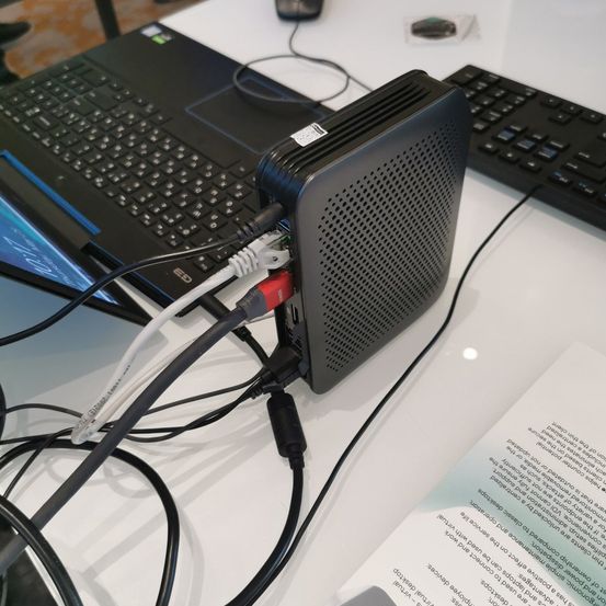 Ein Laptop mit mehreren angeschlossenen Kabeln steht auf einem weißen Tisch mit Tastatur und Maus. Ein Router steht auf dem Tisch mit einigen angeschlossenen Kabeln.