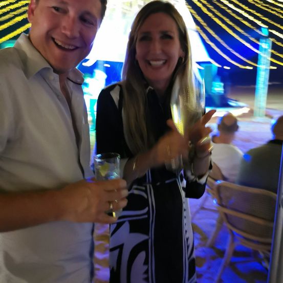 Ein Mann und eine Frau lächeln und halten Weingläser auf einer Strandparty.