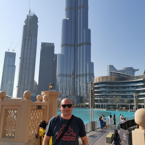 Ein Mann steht vor dem Burj Khalifa, Dubais höchstem Gebäude, mit einem Pool im Vordergrund und anderen Wolkenkratzern im Hintergrund.