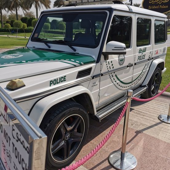 Ein weißer Mercedes G-Wagen Polizeifahrzeug mit grünem Akzent wird auf einem Bürgersteig ausgestellt. Es hat eine rote Seilbarriere und ein Schild, das 'Nicht berühren' sagt.