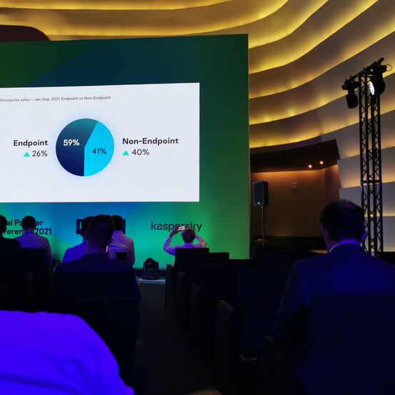 Eine Präsentation mit einem Kreisdiagramm auf einer großen Leinwand zeigt 59% Endpunkt und 41% Nicht-Endpunkt. Mehrere Personen sitzen und beobachten die Präsentation.