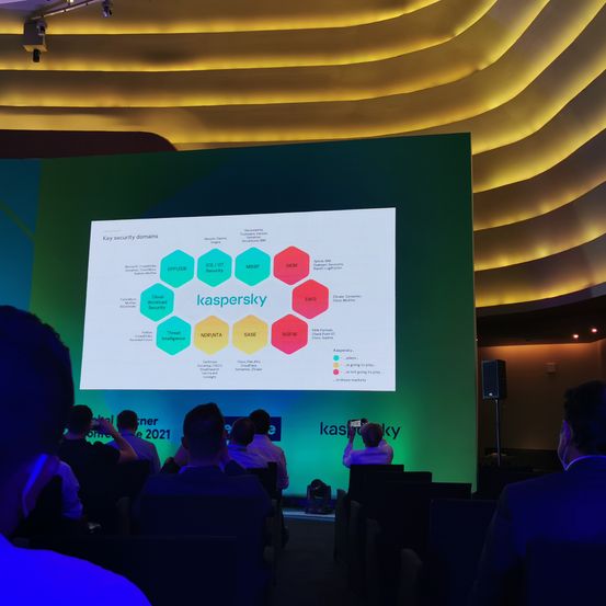 Menschen sitzen vor einer großen Leinwand und sehen sich eine Präsentation von Kaspersky an. Die Leinwand zeigt ein Diagramm der wichtigsten Sicherheitsbereiche.