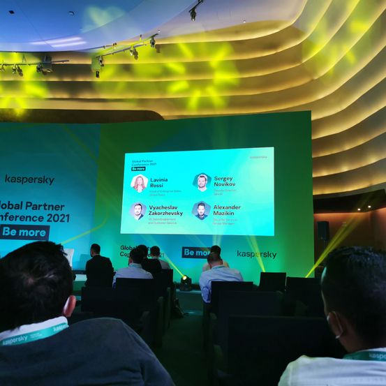 Zuschauer bei der Global Partner Konferenz 2021 von Kaspersky. Redner auf der Bühne mit grünem Hintergrund.