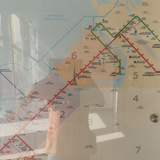 Eine Karte zeigt das Dubai Metro-System, wobei Routen und Stationen mit Nummern und arabischem Text hervorgehoben sind. Es enthält Sehenswürdigkeiten wie Burj Khalifa und Atlantis Aquaventure.