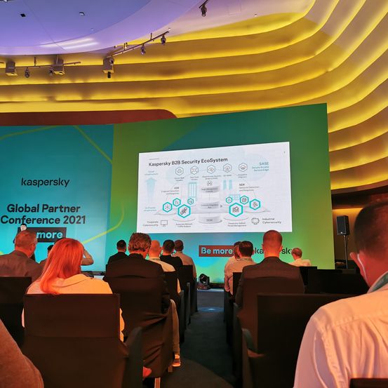 Zuhörer auf einer Konferenz hören eine Präsentation auf einer großen Leinwand, die das Kaspersky B2B Security EcoSystem zeigt. Die Leinwand zeigt ein Diagramm mit verschiedenen Elementen des Systems.