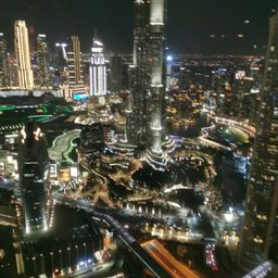 Ein nächtlicher Luftblick auf eine geschäftige Stadt mit vielen Hochhäusern, die von zahlreichen Lichtern erhellt werden, und einem Fluss, der durch die urbane Landschaft fließt.