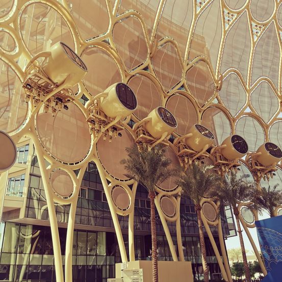 Eine architektonische Gestaltung mit einem goldenen Muster, das kreisförmige Formen und Palmenbäume enthält. Das Gebäude hat Glasfenster und ein goldenes Design.