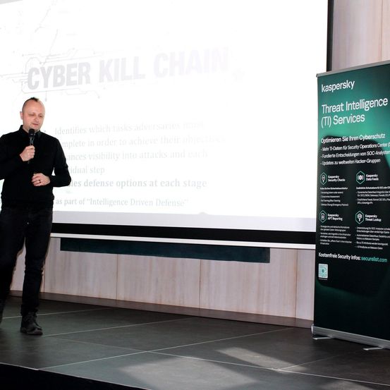 Ein Mann hält eine Präsentation zur Cybersicherheit auf der Bühne, während er neben einem großen Banner steht, das Kaspersky Threat Intelligence (TI) Services bewirbt.