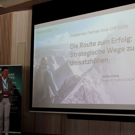 Ein Mann steht vor einer Leinwand mit einer Präsentation mit dem Titel 'Kaspersky Partner Kick-Off 2026'. Die Folie zeigt ein Bild eines Bergsteigers vor einem verschneiten Berghintergrund und Text in deutscher Sprache.