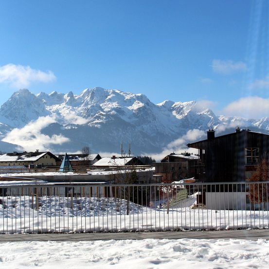 Eine verschneite Stadt mit Blick auf verschneite Berge und blauen Himmel. Die Stadt hat Häuser und Gebäude, die in Schnee bedeckt sind.