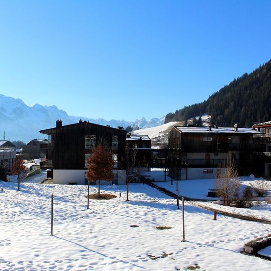 Eine Winterlandschaft mit einer Gruppe von in Schnee bedeckten Chalets, umgeben von einer Bergkette im Hintergrund.