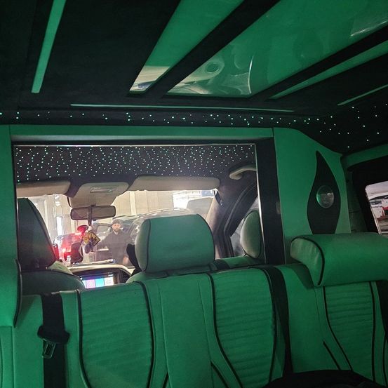 Innenraum eines Luxus-SUV mit grünen Ledersitzen, einem Schiebedach mit sternförmigen Lichtern und der Sicht des Fahrers auf einen Parkplatz.