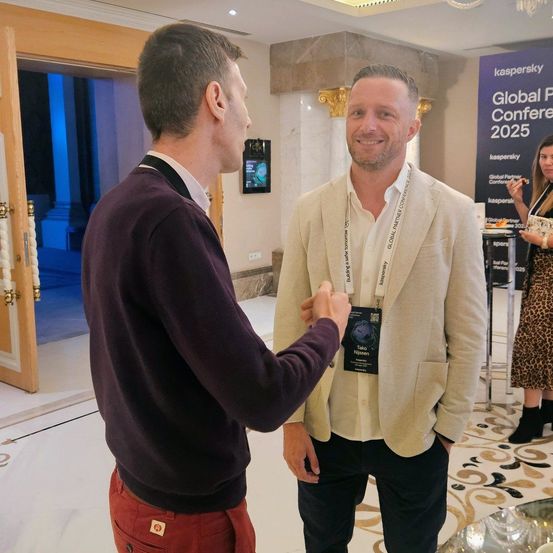 Zwei Männer stehen nebeneinander auf einer Konferenz. Einer schüttelt dem anderen die Hand. Hinter ihnen ist ein Banner für die Global Partner Conference 2025.