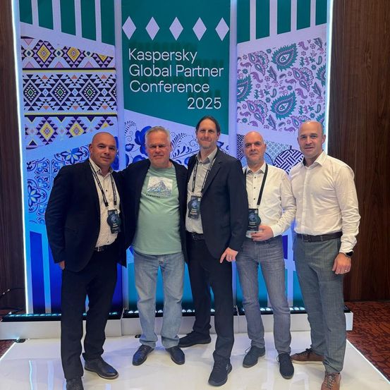 Fünf Männer stehen vor einer Kulisse mit dem Text 'Kaspersky Global Partner Conference 2025'. Sie tragen alle formelle Kleidung und ID-Karten.