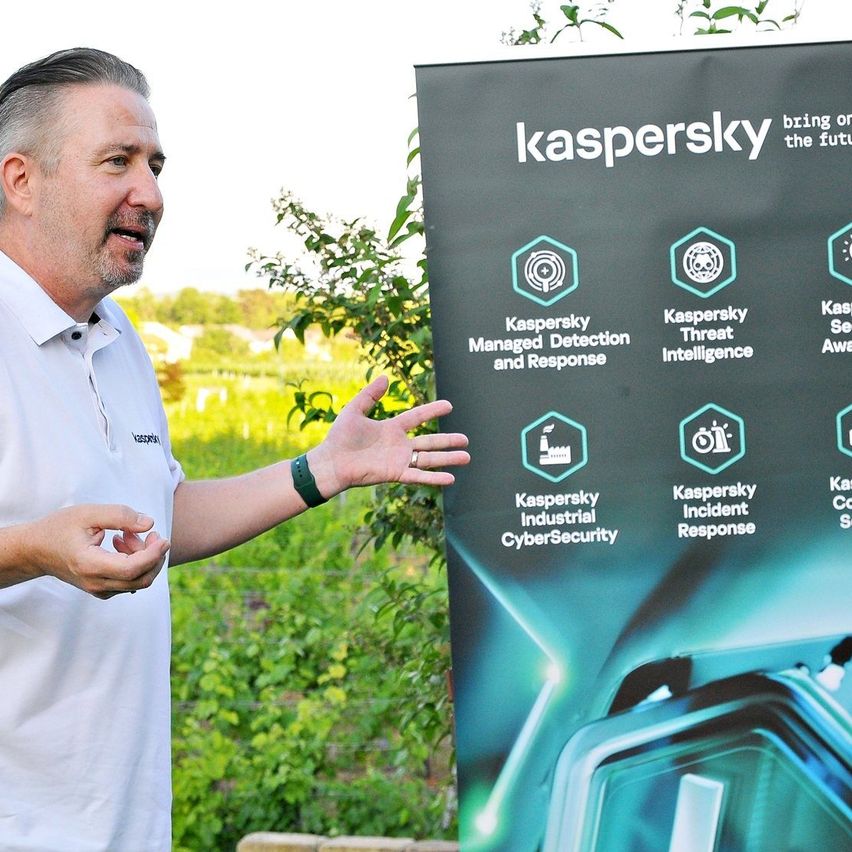 Ein Mann in einem weißen Hemd zeigt auf eine Kaspersky-Werbung. Die Anzeige hebt Funktionen wie Managed Detection, Threat Intelligence und Industrial Cybersecurity hervor.
