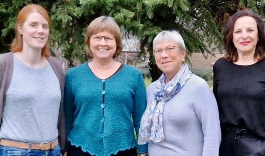 Vier Frauen posieren für ein Foto in einem Garten mit einem Baum im Hintergrund. Sie alle lächeln und scheinen für ein Bild zu posieren.