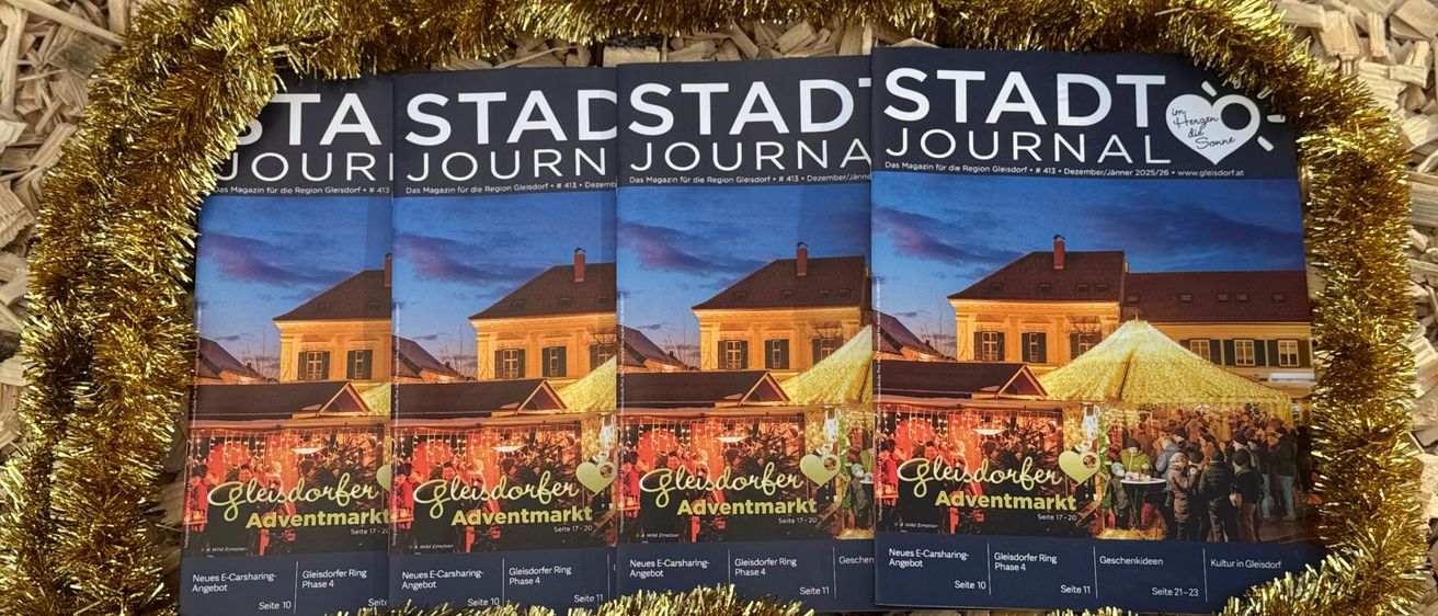 Ein Werbegeschenk-Set der 'Stadt-Stadt Journal'-Magazine, in goldenem Tinselbogen verpackt, auf einem Hintergrund aus Holzspänen.