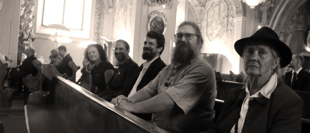 Eine Gruppe von Menschen sitzt in einer Kirche. Ein Mann mit Bart trägt eine Brille.