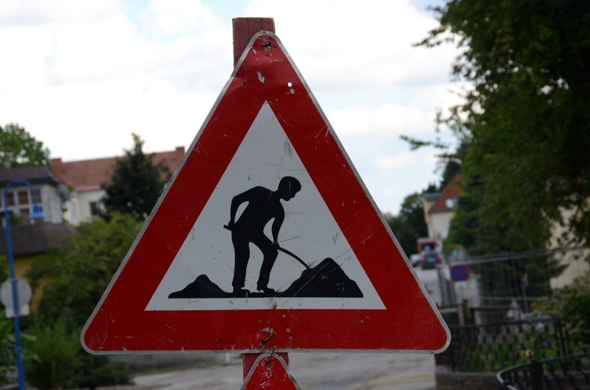 Ein dreieckiges Verkehrsschild mit der Silhouette einer Person, die eine Schaufel hält. Das Schild ist rot und weiß und warnt vor Straßenarbeiten.