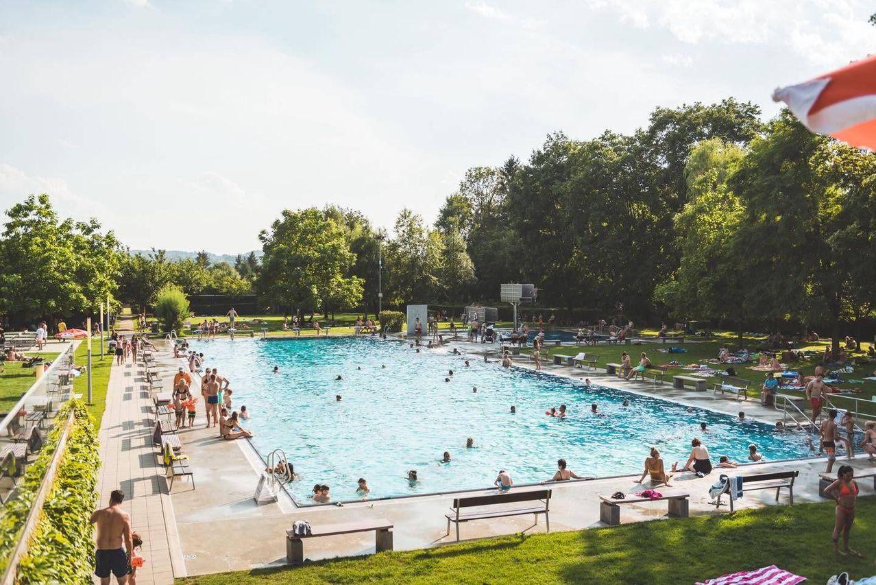 Ein großer Außenpool mit vielen Schwimmern und Leuten, die an einem sonnigen Tag herumlungern.