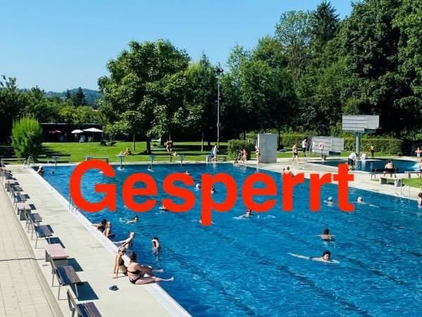 Ein großer Außenpool mit schwimmenden und entspannenden Menschen an den Seiten, umgeben von grünen Bäumen und Gras. Das Wort 'Gesperrt' ist rot über das Bild geschrieben.