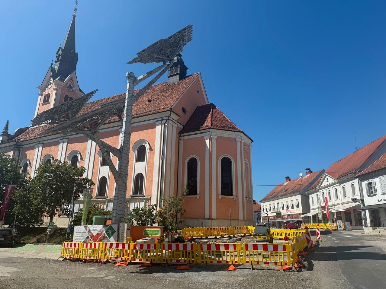 Eine Kirche mit einer großen Solarpanelstruktur auf dem Dach, umgeben von Bauzäunen und einem klaren blauen Himmel.