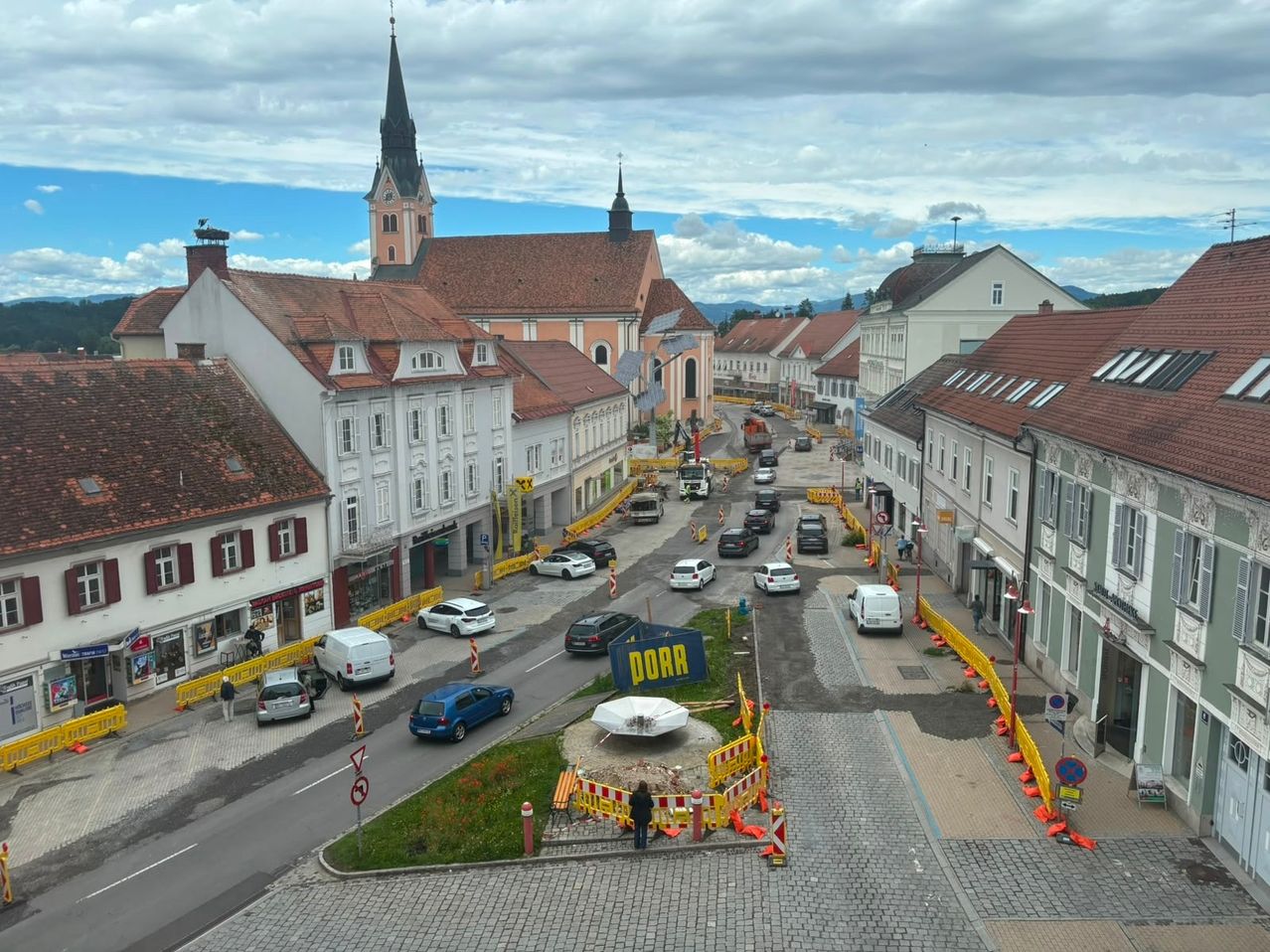 Ein Stadtplatz mit mehreren Gebäuden, Autos und einer Person auf dem Bürgersteig. Ein blaues Schild mit dem Wort Dorr ist in der Mitte.
