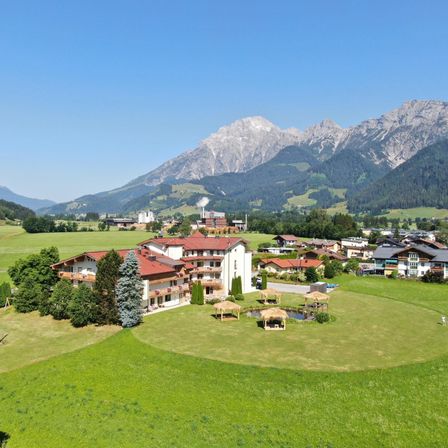 Luftaufnahme eines Resorts mit mehreren Gebäuden, umgeben von üppigem Grün und Bergen im Hintergrund.