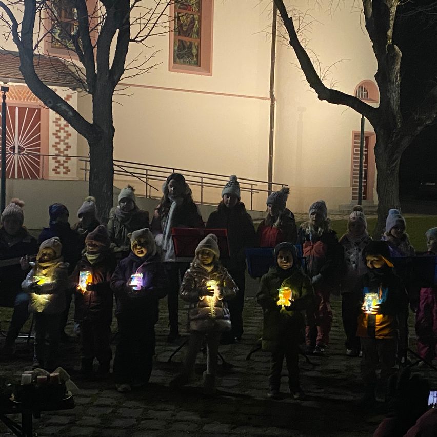 Eine Gruppe von Kindern mit beleuchteten Laternen steht nachts vor einem Gebäude.