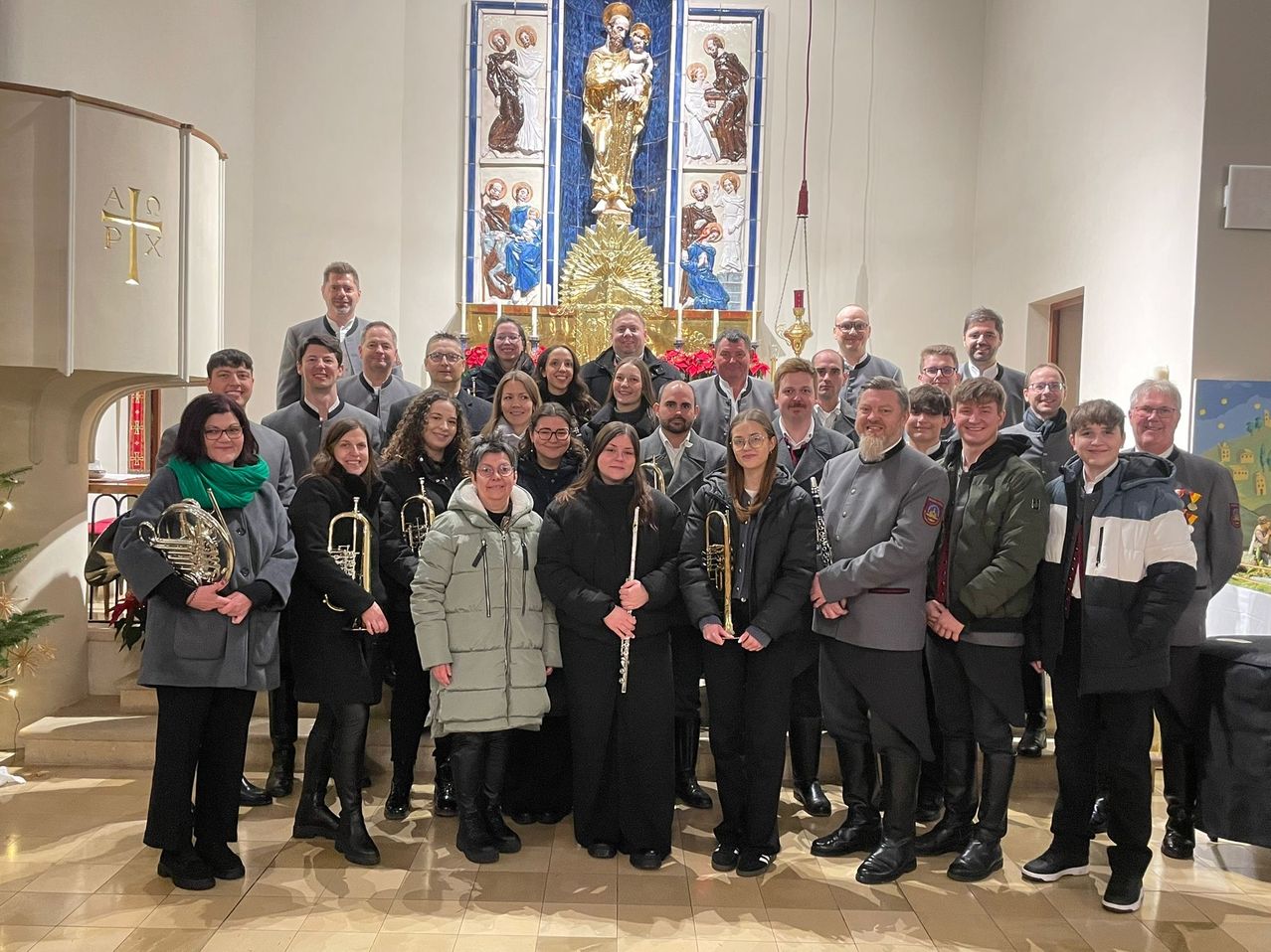 Eine Gruppe von Menschen in Winterkleidung mit Musikinstrumenten posiert für ein Foto vor einem Altar.