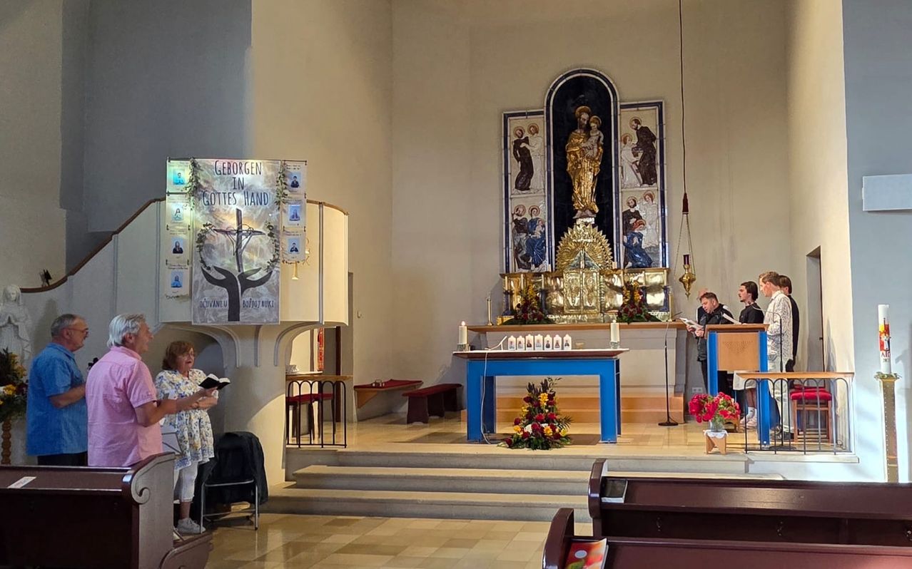 A woman reads a book near a banner in a church. An altar with a statue is at the center. A man reads a book at a podium.