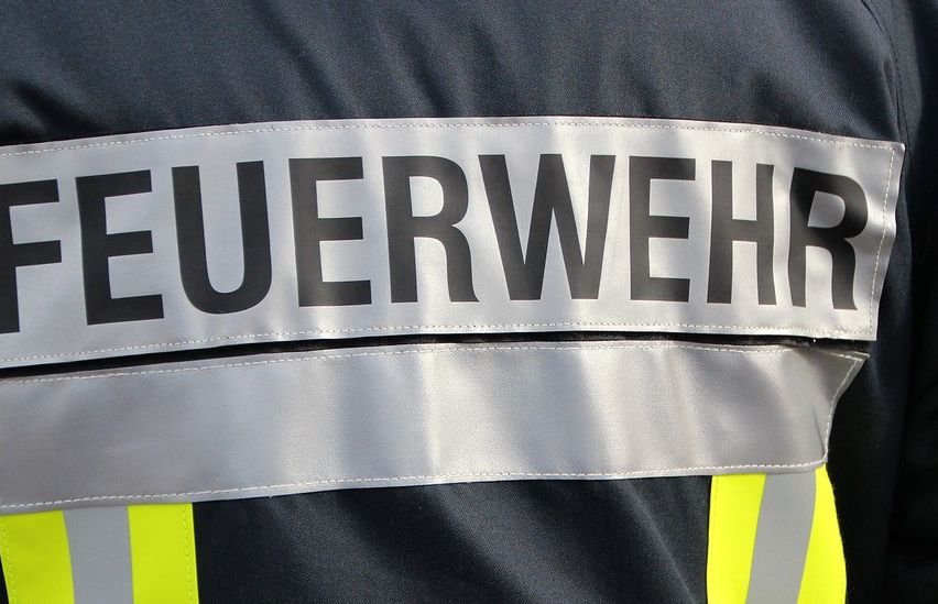 Nahaufnahme der Feuerwehruniform mit dem Wort 'FEUERWEHR' auf dem Rücken. Die Uniform hat reflektierende gelbe und graue Streifen.