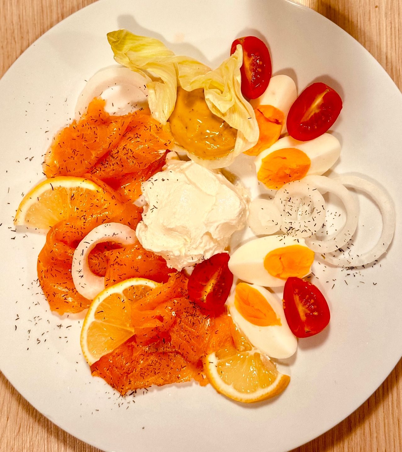 Ein weißer Teller mit Räucherlachs, Zitronenscheiben, Eiern, Zwiebeln und Tomaten.