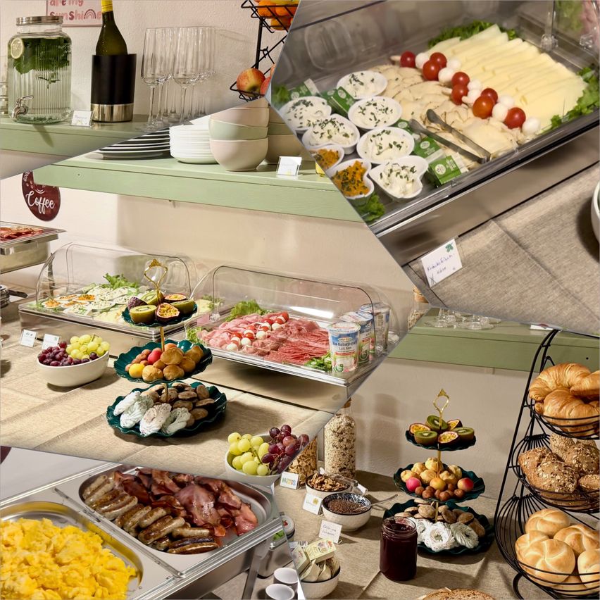 Ein Buffettisch mit verschiedenen Speisen wie Würstchen, Eiern, Obst und Brot, zusammen mit Weingläsern und einer Flasche Wein.