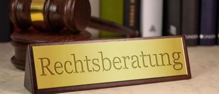 Ein hölzerner Richterhammer liegt auf einem Schild, das 'Rechtsberatung' in goldenen Buchstaben vor einer Reihe von Büchern zeigt.