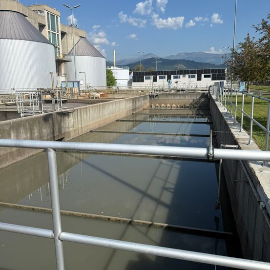 Eine Wasseraufbereitungsanlage mit großen Tanks und einem Metallgeländer, unter einem klaren blauen Himmel mit Bergen in der Ferne.