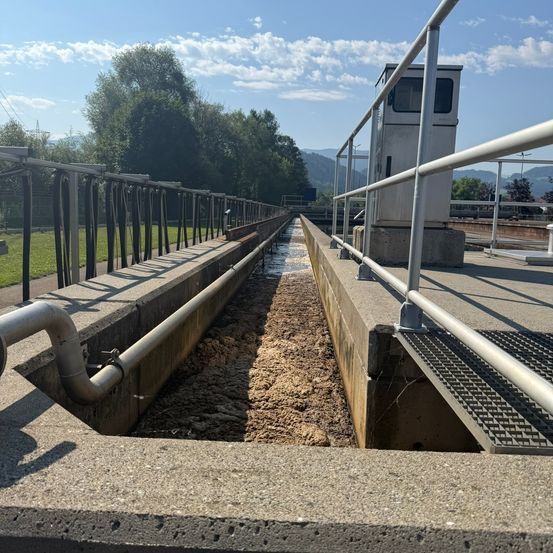Eine Wasseraufbereitungsanlage mit einem Betonkanal und einem Metallgeländer unter einem teilweise bewölkten Himmel.