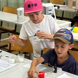 Zwei Jungen führen ein wissenschaftliches Experiment in einem Klassenzimmer durch. Ein Junge hält eine Pipette und ein Reagenzglas, während der andere Junge ein kleines Glas und eine Kerze hält.