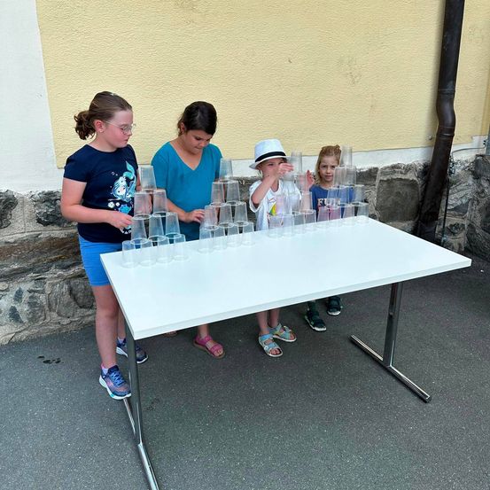 Vier Kinder stehen um einen Tisch mit gestapelten Bechern herum, möglicherweise spielen sie ein Spiel.