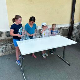 Vier Kinder stehen um einen Tisch mit gestapelten Bechern herum, möglicherweise spielen sie ein Spiel.