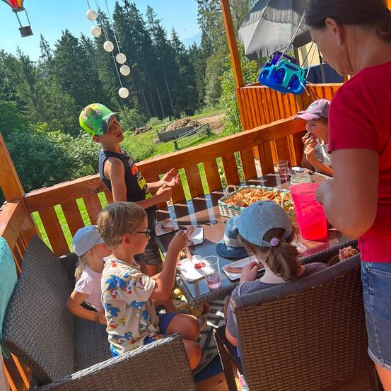 Eine Familie isst auf einer Veranda mit Blick auf einen Heißluftballon und Bäume.
