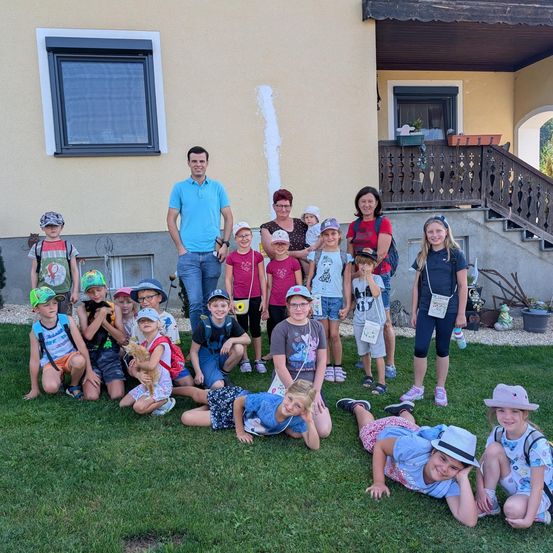 Eine Gruppe von Kindern und Erwachsenen posiert für ein Foto vor einem Haus. Einige knien, andere stehen, und eine Person hält eine Katze.