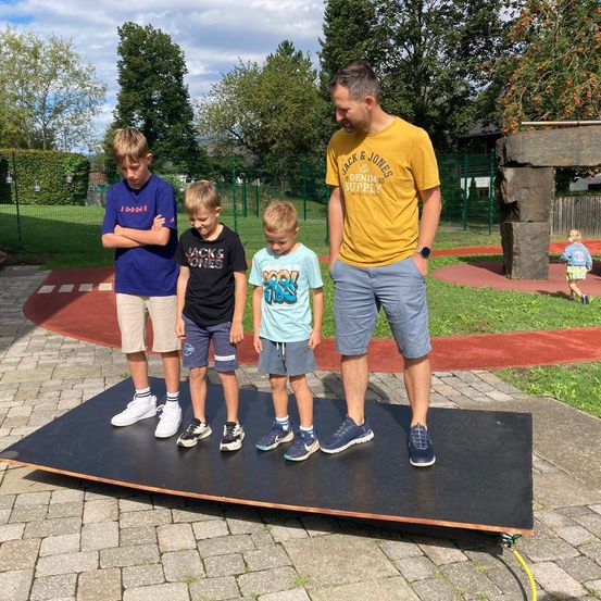 Ein Mann und drei Jungen stehen auf einem schwarzen Teppich im Park, wobei ein Junge die Arme verschränkt.