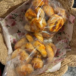 Zwei Plastiktüten mit goldbraunen, leicht verbrannten Brötchen in einem geflochtenen Korb mit einem Blumentuch darunter.
