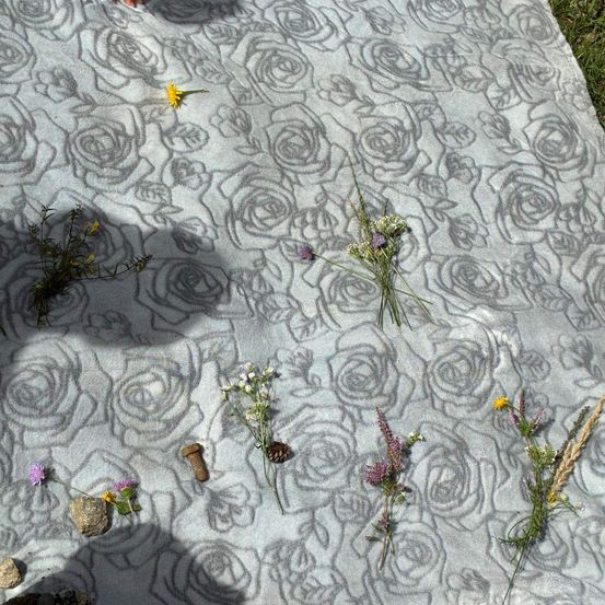 Eine graue, blumengemusterte Decke mit verschiedenen kleinen Blumen und einem Korken verstreut.