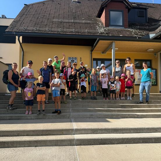Eine Gruppe von Erwachsenen und Kindern steht auf den Stufen eines Gebäudes und lächelt für ein Foto.