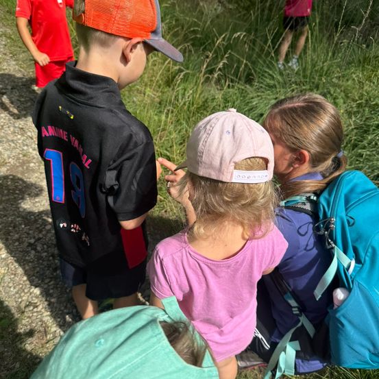 Eine Gruppe von Kindern im Freien, eines trägt ein schwarzes Shirt mit der Nummer 18, ein anderes eine rosa Mütze und ein Mädchen mit einem blauen Rucksack.