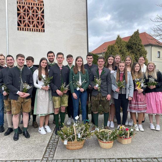 Eine Gruppe von Menschen in traditioneller Kleidung, die vor einem Gebäude mit einem Korb voller Blumen für ein Foto posiert.